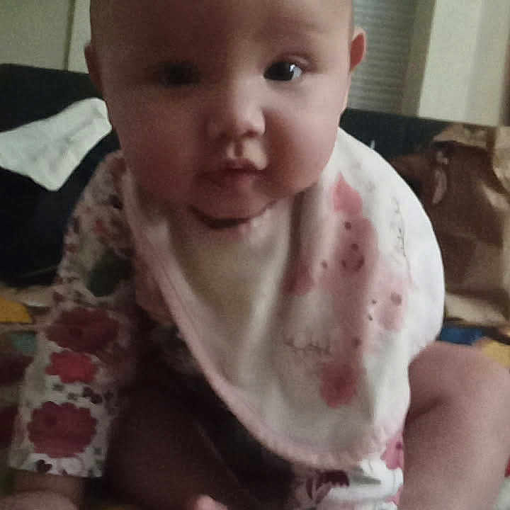 Roselyne joined the competition — help win amazing prizes! baby, bib, blanket, child, curious, cute, eyes, face, feet, floral_clothing, front_view, hands, head, indoors, infant, person, portrait, sitting, soft_lighting, young