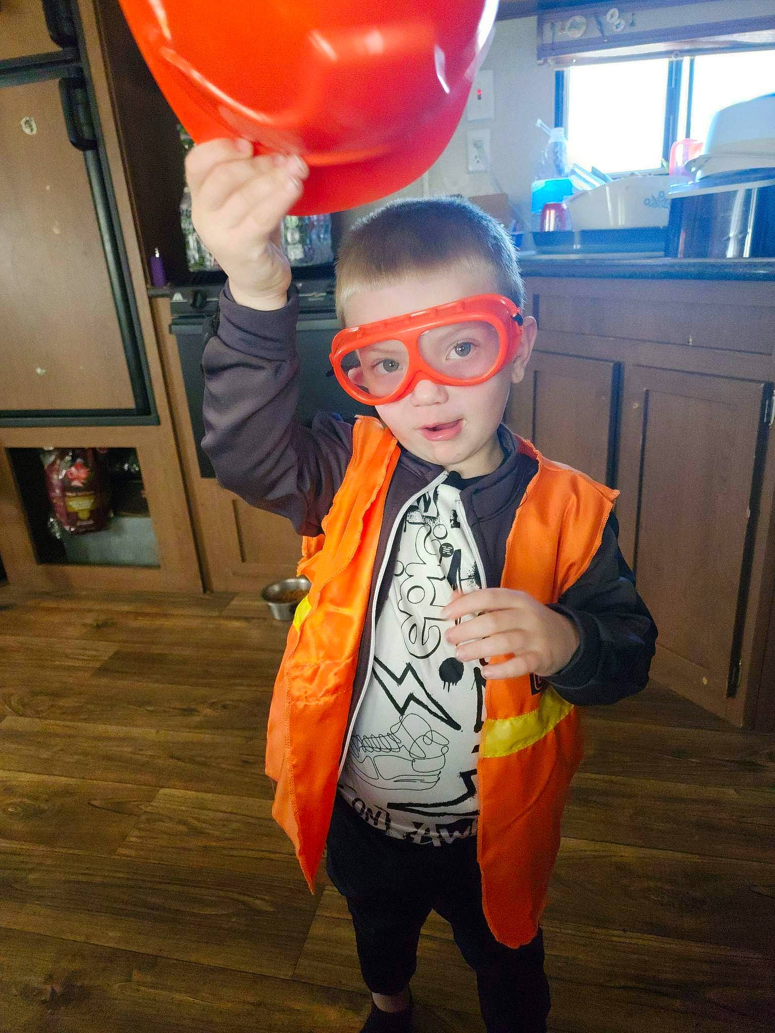 Preston is registered to the contest to win money with this photo: animation, balloon, cabinetry, child, costume, event, eyewear, flooring, fun, human_body, orange, party, party_supply, person, personal_protective_equipment, room, standing, t_shirt, television, toddler