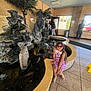 Nathaly joined the competition — help win amazing prizes! child, girl, indoor, water_feature, fish_statue, rocks, purple_dress, sunglasses, floor_tiles, window, entrance, statue, people, water, plant, door, handbag, shoes, lighting, reflection