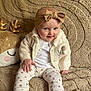 baby, child, infant, headband, bow, sweater, leggings, shoes, plush_toy, blanket, beige, patterned_clothing, smiling, sitting, cute, indoors, cozy, soft_texture, person, portrait