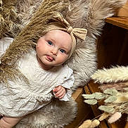 Romane participe au concours pour gagner de l'argent avec cette photo : baby, child, infant, headband, tongue_out, fur_rug, dried_plants, beige, white_clothing, wooden_floor, wooden_furniture, cute, playful, portrait, indoor, soft_texture, cozy, natural_colors, smiling, person