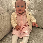 Emerie is registered to the contest to win money with this photo: baby, cardigan, child, clothing, couch, cozy, cute, happy, hat, indoors, infant, person, pink_dress, portrait, seated, smiling, socks, sofa, textured_fabric, tights