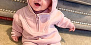 Mabel is registered to the contest to win money with this photo: baby, child, pink_clothing, hoodie, pants, sitting, carpet, indoor, smiling, happy, face, blue_eyes, cozy, fleece, furniture, couch, home, cute, young_child, portrait