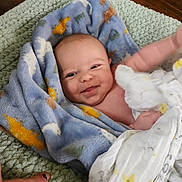 Peyton joined the competition — help win amazing prizes! baby, blanket, smiling, infant, face, hand, nail_polish, blue_blanket, patterned_blanket, soft_texture, green_surface, wrapped, cute, child, skin, happy, indoors, closeup, person, toddler