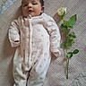 baby, infant, onesie, pink_clothing, blanket, flower, rose, leaf, greenery, texture, lying_down, cute, peaceful, soft, indoors, portrait, face, newborn, sleepwear, resting