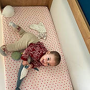 Prune participe au concours pour gagner de l'argent avec cette photo : baby, bed, beige_pants, child, cozy, crib, cute, fabric, happy, heart_pattern, indoor, infant, knitted_toy, person, playful, red_sweater, sleeping_area, smiling, soft_toys, toy