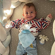 Lucien participe au concours pour gagner de l'argent avec cette photo : baby, child, smiling, striped_sweater, denim, toy, teddy_bear, comforter, braided_cushion, bed, playful, cozy, indoor, cute, infant, sock, face, person, happy, star_patterned_bed