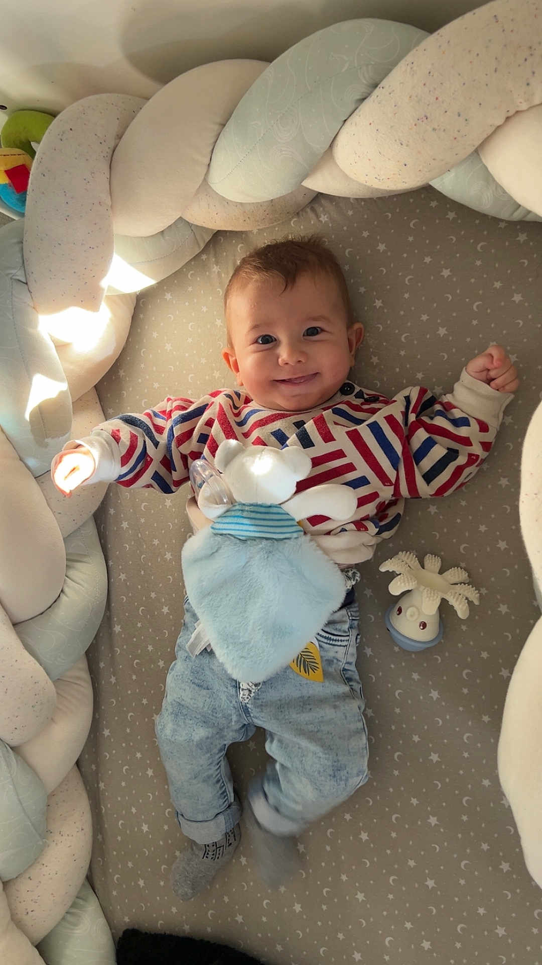 Lucien participe au concours pour gagner de l'argent avec cette photo : baby, child, smiling, striped_sweater, denim, toy, teddy_bear, comforter, braided_cushion, bed, playful, cozy, indoor, cute, infant, sock, face, person, happy, star_patterned_bed