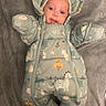 Nalani is registered to the contest to win money with this photo: baby, infant, snowsuit, dinosaur_pattern, blanket, soft_texture, cute, lying_down, hooded, warm_clothing, child, indoor, floor, playful, smiling, face, person, cozy, winter_wear, adorable