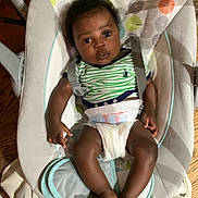 Usyah Hall joined the competition — help win amazing prizes! baby, infant, child, diaper, striped_shirt, baby_rocker, cushion, seat, floor, wood_floor, indoor, person, baby_clothing, curly_hair, looking, hands, feet, calm, colorful, patterned