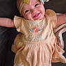 Davina is registered to the contest to win money with this photo: baby, smiling, headband, dress, peach_color, embroidery, lying_down, blanket, cute, child, infant, happy, apparel, person, indoors, fabric, face, skin, toddler, portrait