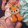 baby, blanket, child, comfort, couch, cozy, cute, fabric, indoors, infant, orange_toy, pacifier, person, pink_clothing, plush_toy, relaxed, resting, sleepy, small, soft_toy