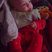 Davina is registered to the contest to win money with this photo: baby, bib, blanket, child, comfort, couch, cozy, face, head, indoor, infant, pajamas, person, plush, red_clothing, relaxing, seated, soft_toy, stuffed_toy, warm_lighting