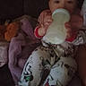 Davina is registered to the contest to win money with this photo: baby, infant, child, bottle, feeding, pajamas, cartoon, blanket, purple_blanket, plush_toy, sitting, lounging, indoor, dim_lighting, portrait, face, eyes, hands, cozy, sleepy