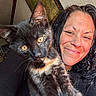 cat, tortoiseshell_cat, woman, person, selfie, portrait, smiling, indoor, pet, animal, feline, whiskers, green_eyes, fur, black_fur, orange_fur, nose_ring, black_clothing, close_up, home