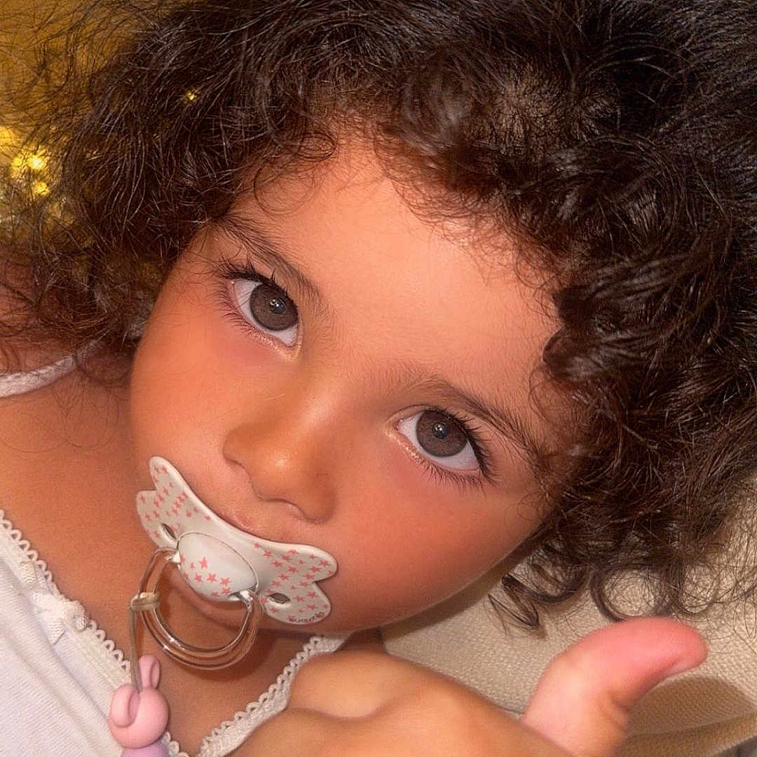 Numidia a rejoint le concours — aidez-le/la à gagner de superbes lots ! baby_accessory, beads, child, close_up, clothing, curly_hair, cute, expression, face, hand, indoor, pacifier, person, portrait, seated, skin, soft_lighting, thumbs_up, toddler, young_child