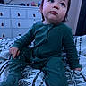toddler, child, baby, sitting, portrait, face, eyes, brown_hair, green_outfit, jumpsuit, bed, bedroom, dresser, television, indoors, home, blanket, patterned_bedding, serious_expression, photography