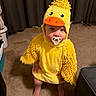 Aubrey joined the competition — help win amazing prizes! baby, child, duck_costume, yellow, fluffy, pacifier, portrait, indoors, living_room, carpet, curtains, costume, cute, sitting, standing, infant, face, eyes, home, humorous
