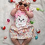 baby, child, sunglasses, headband, bow, blanket, easter_eggs, pink_clothing, floral_pattern, bunny_design, pastel_colors, cute, infant, laying_down, decorations, holiday, celebration, soft_texture, footwear_free, happy