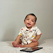 Ayansh is registered to the contest to win money with this photo: baby, infant, child, smile, sitting, shirt, patterned_shirt, bracelet, tablet, reflection, bed, blanket, indoors, plain_wall, toes, feet, portrait, happy, cute, photography