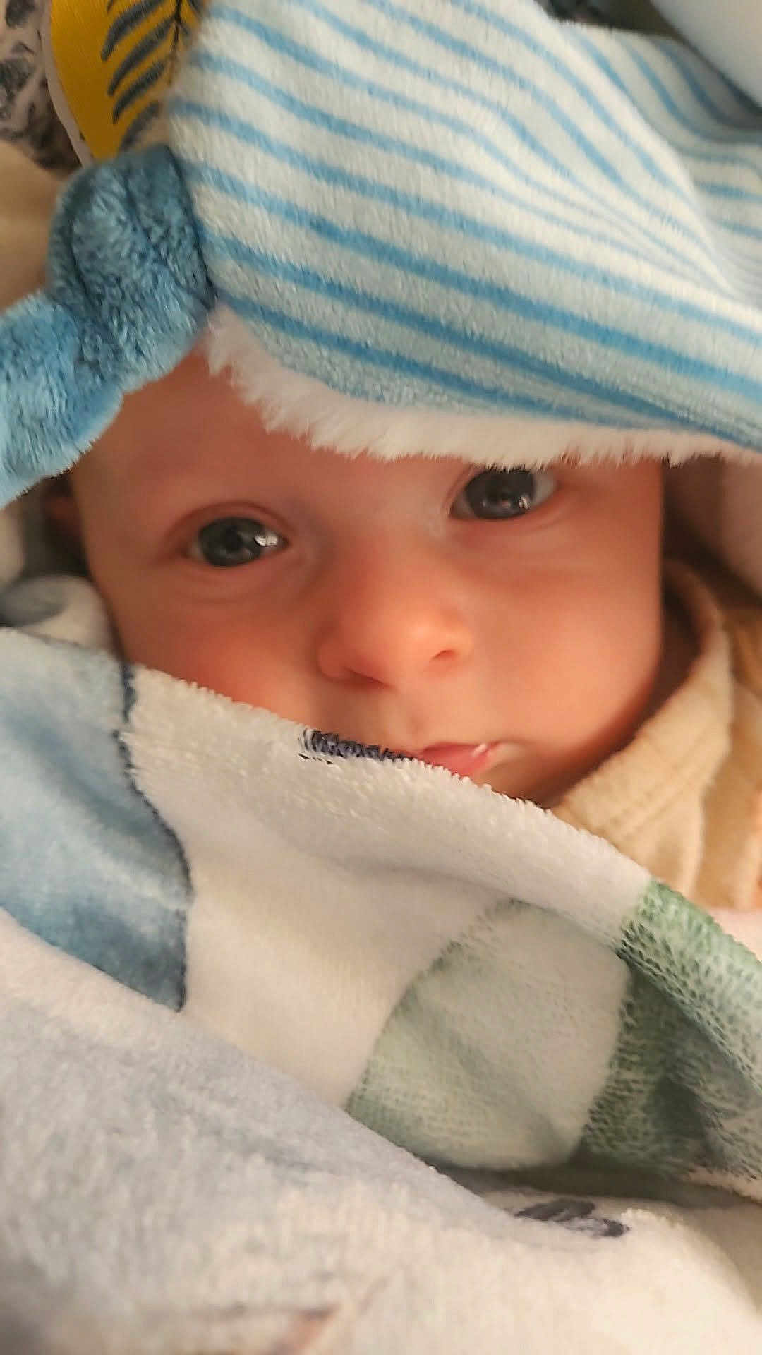 Louis a rejoint le concours — aidez-le/la à gagner de superbes lots ! baby, infant, child, blanket, towel, striped_hat, closeup, portrait, eyes, face, nose, mouth, drool, cozy, soft_texture, fabric, wrapped, indoor, cute, sleepy