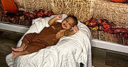 Ryan joined the competition — help win amazing prizes! baby, child, infant, smiling, portrait, lying_down, blanket, overalls, brown_clothing, pumpkins, autumn, fall, hay_bale, string_lights, decorations, leaves, indoor, wooden_wall, wood_floor, cozy