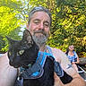 Jinx is registered to the contest to win money with this photo: man, cat, black_cat, harness, outdoor, canoe, water, forest, trees, sunlight, woman, paddling, smiling, nature, summer, adventure, animal, pet, happy, daytime