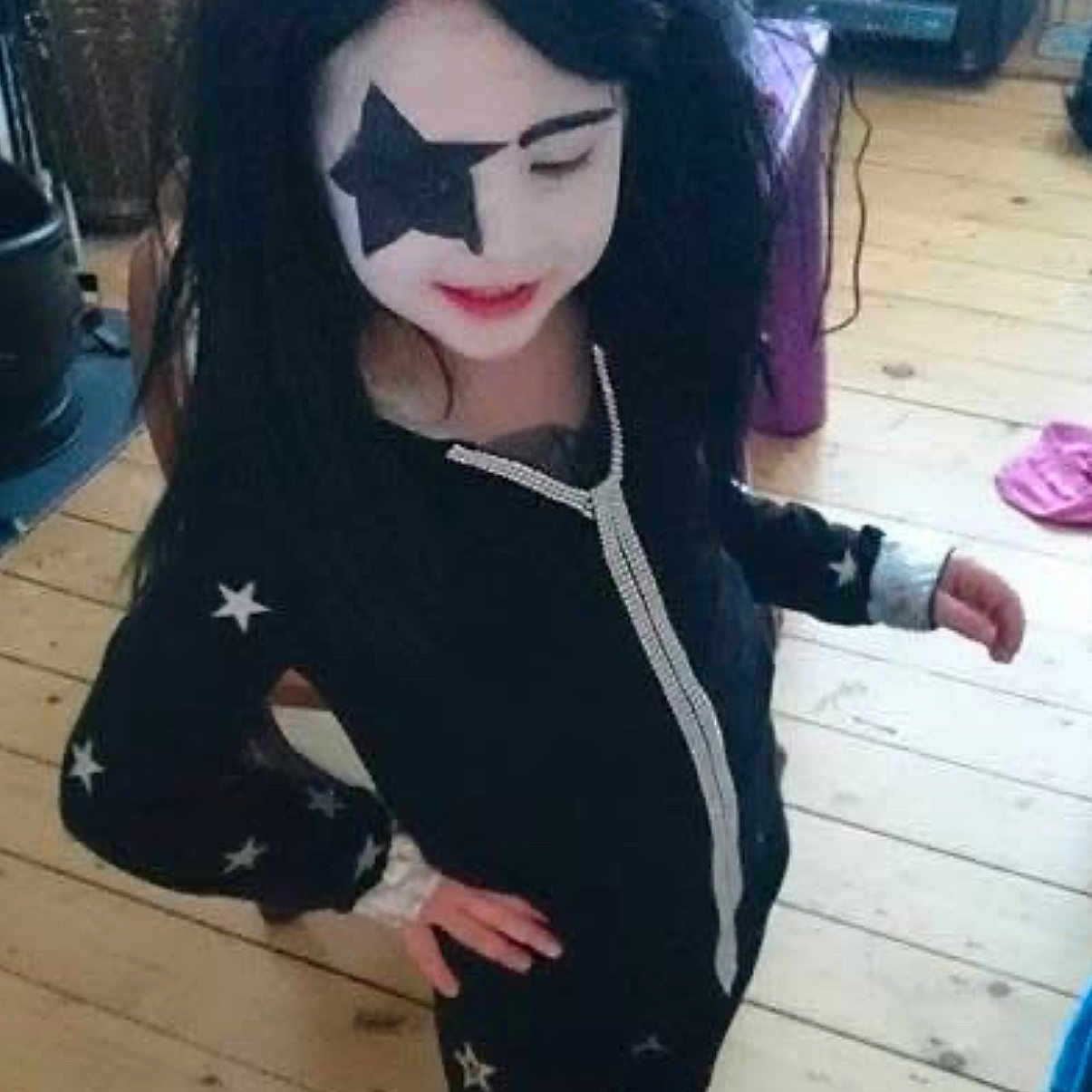 Lucie Adams joined the competition — help win amazing prizes! child, face_paint, star, black_hair, costume, indoor, wooden_floor, hand_on_hip, long_sleeves, pants, footwear, furniture, basket, printer, pink_slippers, purple_object, black_outfit, white_face, smile, pose