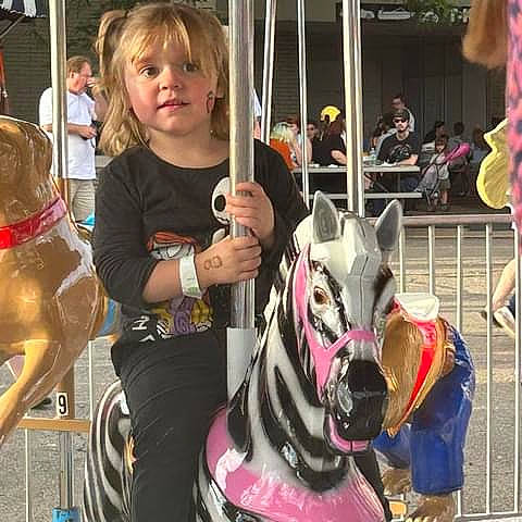 Raelea is registered to the contest to win money with this photo: amusement_ride, blurred, bridle, carousel, child, event, fun, horse_supplies, horse_tack, leisure, mammal, nonbuilding_structure, pack_animal, person, public_event, recreation, snapshot, snout, t_shirt, toddler