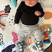 Zeke joined the competition — help win amazing prizes! baby, black_clothing, child, colorful, cute, expression, face, floor, grey_pants, indoor, infant, lying_down, pattern, person, play_mat, playtime, socks, soft_toys, toy, wooden_floor