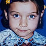 child, portrait, blue_eyes, hair_clip, dress, lace_collar, patterned_clothing, close_up, smile, young_girl, face, innocence, dark_hair, blue_background, fashion, cute, eyelashes, childhood, studio_photo, headshot