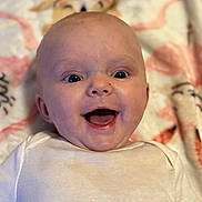 Willow is registered to the contest to win money with this photo: baby, blanket, child, closeup, cute, expression, face, happy, head, indoors, infant, lying_down, mouth_open, one_person, patterned_blanket, portrait, skin, smile, white_clothing, young_child