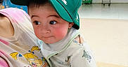 Tobias is registered to the contest to win money with this photo: baby, child, person, cap, hat, green_cap, tshirt, cartoon_print, indoor, locker, cart, floor, curious, holding, shorts, clothing, headwear, cute, face, human