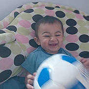 Tobias is registered to the contest to win money with this photo: baby, child, smiling, happy, soccer_ball, toy, polka_dot, blanket, pattern, indoor, cute, playful, seated, person, head, face, clothing, blue, white, hand