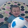 baby, child, smiling, happy, soccer_ball, toy, polka_dot, blanket, pattern, indoor, cute, playful, seated, person, head, face, clothing, blue, white, hand