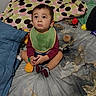 toddler, child, baby, bed, blanket, pillow, toy, bib, socks, indoor, cute, cross_legged, expression, looking_up, patterned, colorful, soft_toys, casual_clothing, floor_bedroom, home