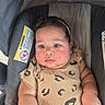 adorable, baby, car_seat, cheeks, child, close_up, clothing, earring, eyes, face, headband, indoors, infant, looking_at_camera, patterned_outfit, photograph, portrait, safety_label, sitting, stroller