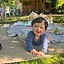 baby, child, outdoor, grass, mat, toys, blanket, wooden_shed, sunlight, smiling, crawling, nature, greenery, person, happy, clothing, playtime, daylight, face, head