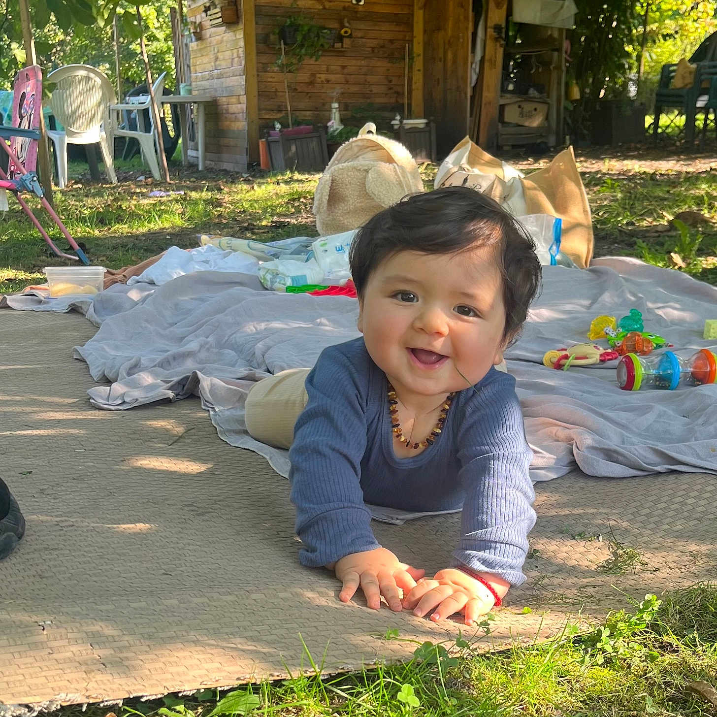 Isidor participe au concours pour gagner de l'argent avec cette photo : baby, blanket, child, clothing, crawling, daylight, face, grass, greenery, happy, head, mat, nature, outdoor, person, playtime, smiling, sunlight, toys, wooden_shed