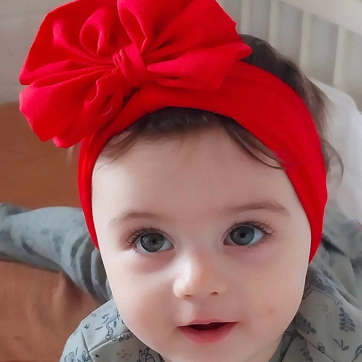 Margaux participe au concours pour gagner de l'argent avec cette photo : baby, bed, bedding, child, closeup, clothing, cute, expression, eyes, face, hair, headband, indoors, infant, person, portrait, red_bow, skin, smile, young