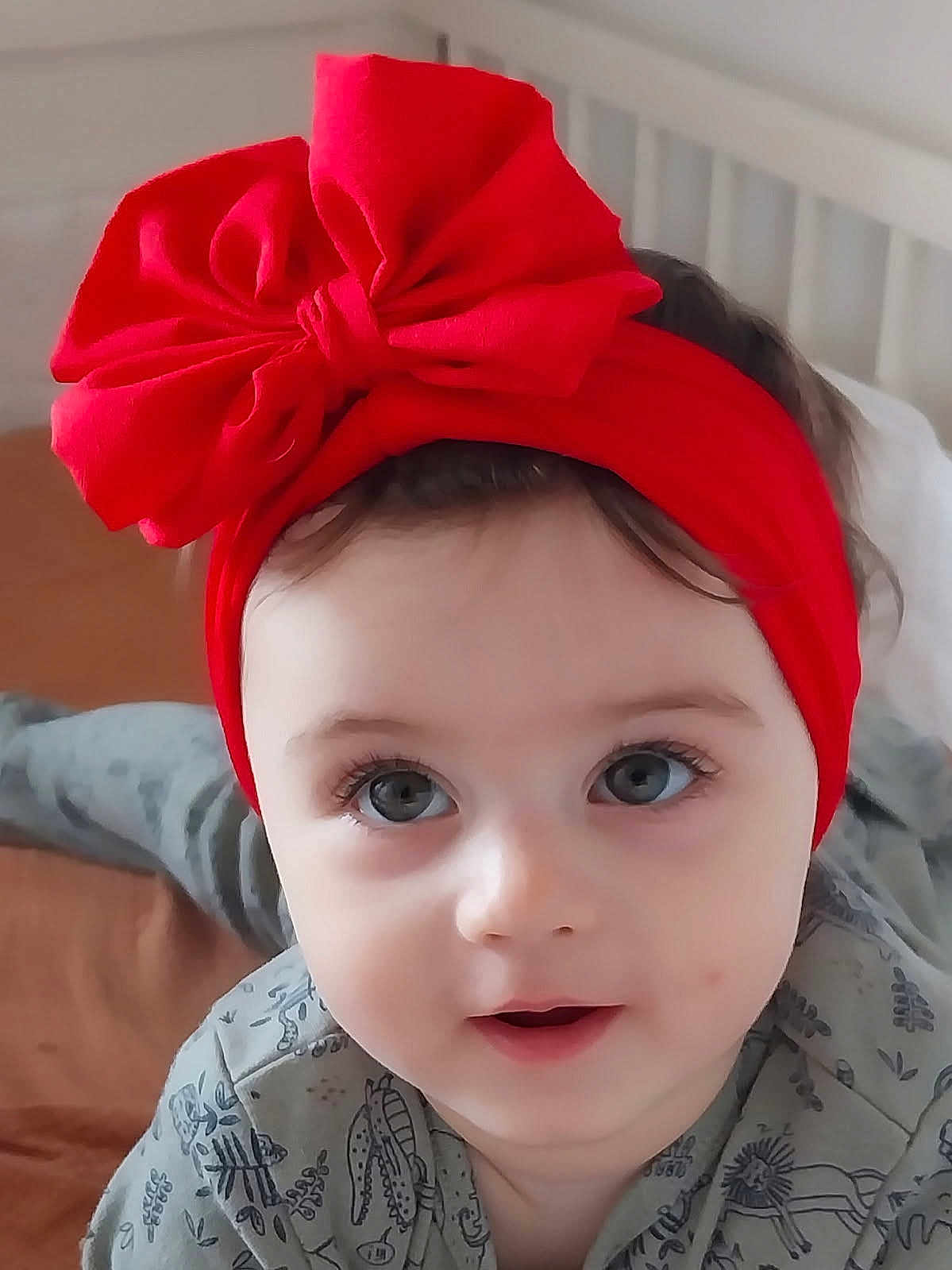Margaux participe au concours pour gagner de l'argent avec cette photo : baby, child, face, headband, red_bow, eyes, infant, cute, portrait, bed, bedding, clothing, expression, skin, hair, indoors, person, young, smile, closeup