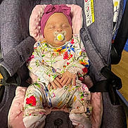 Eden is registered to the contest to win money with this photo: baby, infant, sleeping, pacifier, car_seat, headband, bow, floral_clothing, pink, purple, hands, footed_pajamas, soft_padding, indoor, child, cute, resting, peaceful, person, newborn