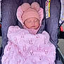 baby, sleeping, stroller, blanket, knit_hat, pom_poms, pink, gray, cozy, child, infant, outdoor, warm_clothing, soft_texture, car_seat, warning_label, cute, peaceful, portrait, bundle