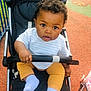 baby, child, stroller, outdoor, curious, infant, playground, person, clothing, socks, pants, shirt, hand, face, eyes, hair, seat, toy, play_area, daytime