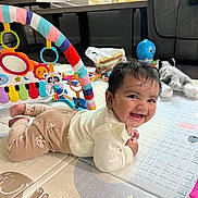 Eshani Reddy joined the competition — help win amazing prizes! baby, smiling, play_mat, toys, stuffed_animal, living_room, child, floor, colorful, cute, happy, infant, clothing, person, indoor, playtime, piano_toy, soft_toys, head, face