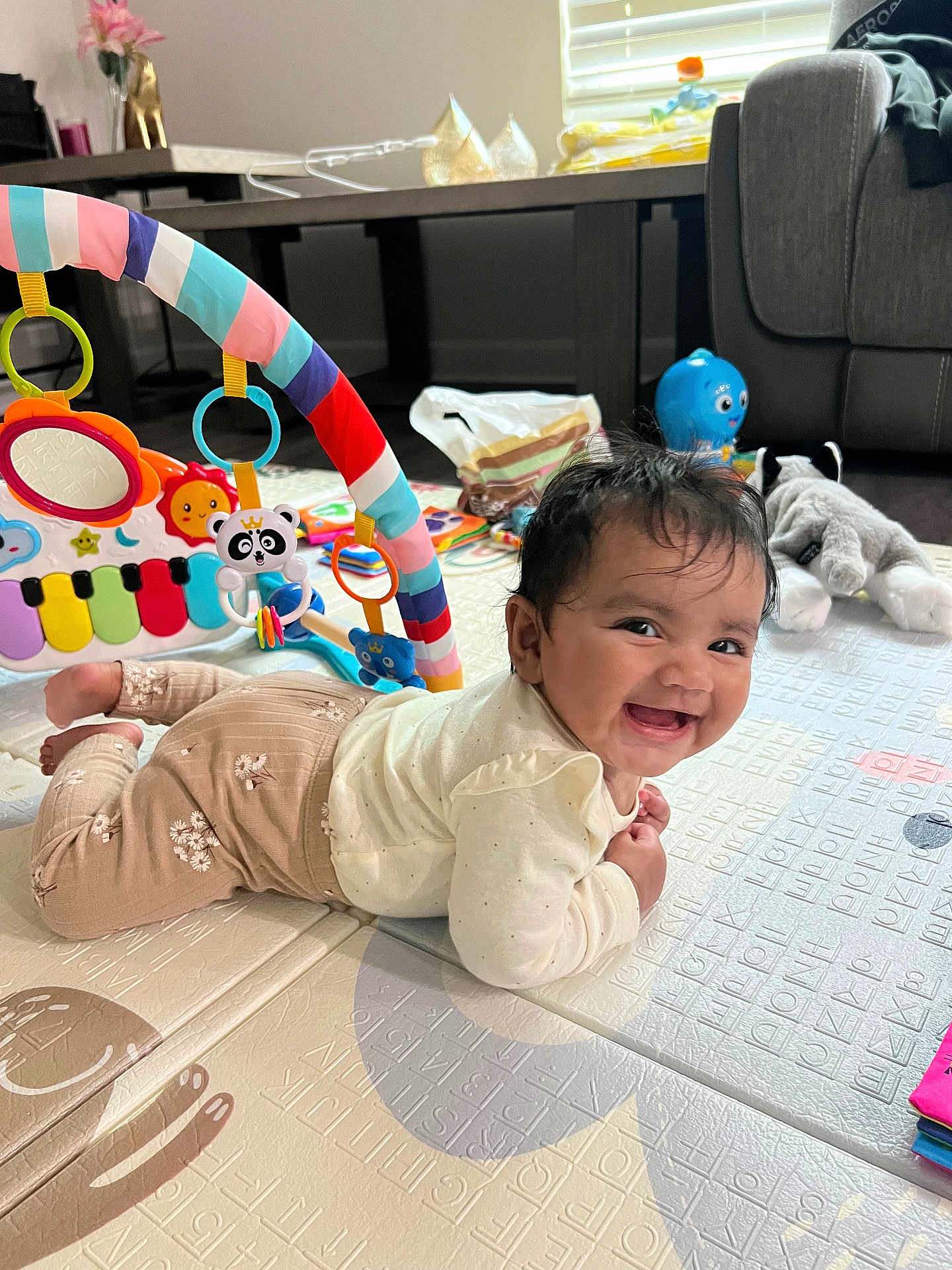 Eshani Reddy joined the competition — help win amazing prizes! baby, smiling, play_mat, toys, stuffed_animal, living_room, child, floor, colorful, cute, happy, infant, clothing, person, indoor, playtime, piano_toy, soft_toys, head, face