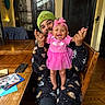 Marisol is registered to the contest to win money with this photo: baby, child, man, smile, happy, pink_dress, headband, beanie, tattoo, wooden_table, chair, indoor, person, clothing, face, hand, home_interior, cabinet, phone, cards