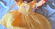 Marisol is registered to the contest to win money with this photo: baby, child, smile, yellow_dress, hair_bows, white_socks, lying_down, bed_sheet, happy, infant, portrait, cute, raised_arms, fabric_texture, indoors, person, skin, face, clothing, playful