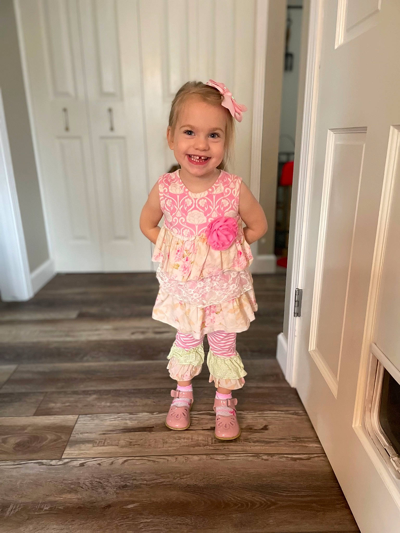 Brynn is registered to the contest to win money with this photo: arm, baby_toddler_clothing, door, dress, eye, face, floor, flooring, happy, hardwood, head, human_body, joy, person, pink, product, sleeve, smile, standing, toddler