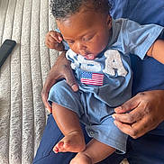 Kyaire joined the competition — help win amazing prizes! baby, child, person, curly_hair, blue_clothing, american_flag, sitting, hands, adult, couch, remote_control, indoor, feet, legs, close_up, supporting, curious, casual, home, comfort